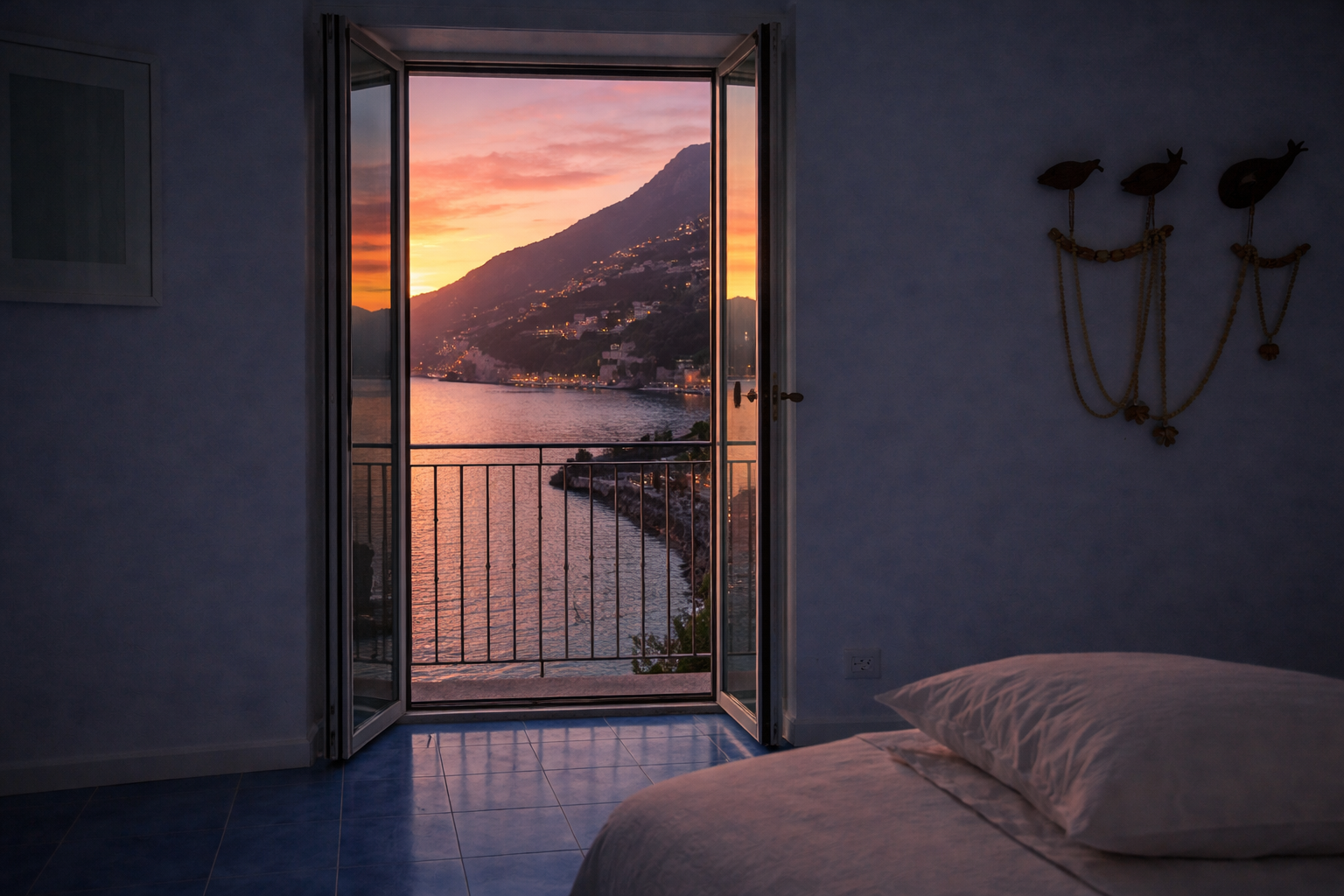 Camera da letto di AMALFI Sea House con porta aperta sul balcone al tramonto infuocato sulla costa amalfitana