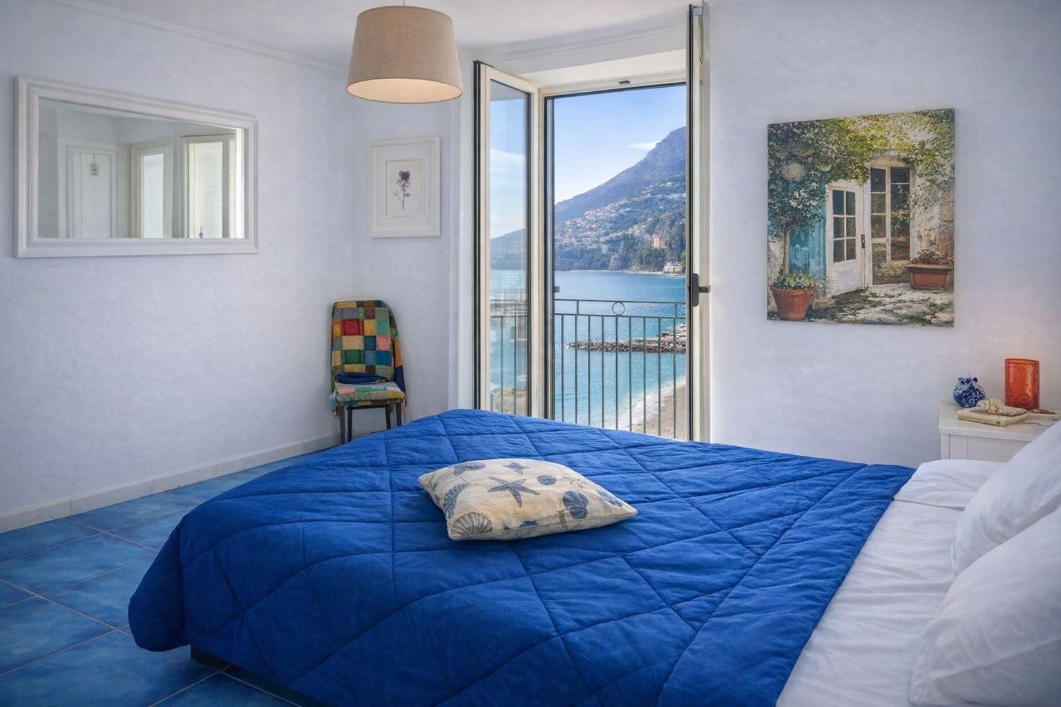 Camera da letto di AMALFI Sea House con letto matrimoniale blu, pavimento in maiolica e porta-finestra aperta sul mare cristallino della Costiera Amalfitana