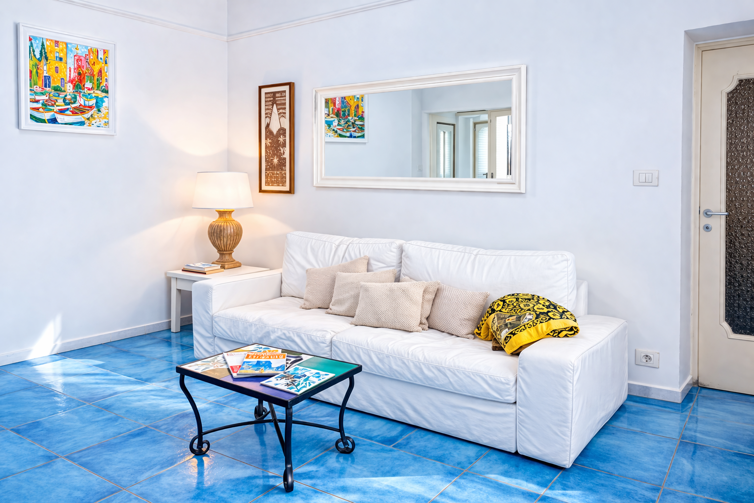 Soggiorno luminoso di AMALFI Sea House con divano bianco, pavimento in maiolica blu e quadri artigianali amalfitani